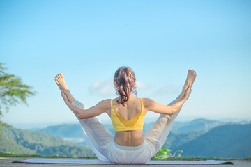 Young woman doing exercise yoga. sitting on mat doing wide legged boat pose. Amazing yoga landscape...