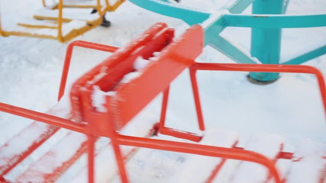 Girl spinning on carousel in playground at winter. Girl riding carousel swing and losing wallet from pocket on snowy children playground