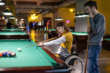 Beautiful disabled girl in a wheelchair playing billiards with her friend