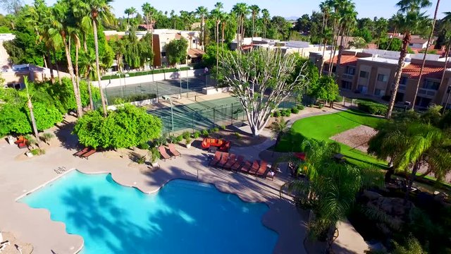 Aerial drone photography over a nice pool with palm trees and tennis courts. subtle camera movement gives the clip a cool look