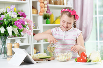 Cute girl preparing delicious fresh salad in kitchen