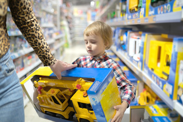 A little child with mother chooses a toy car in the store