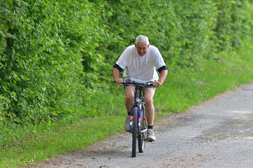 An older man is cycling on bike on a forest road in summer