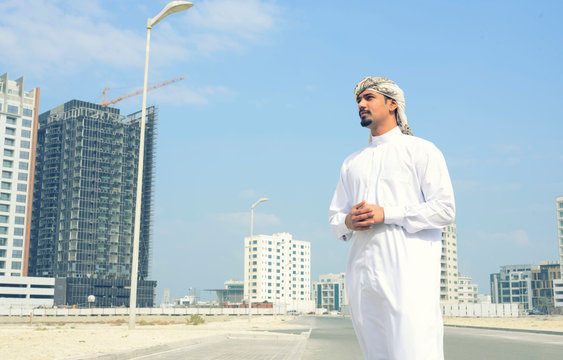 Business middle east man wearing white traditional dress with turban standing outdoor with buliding projects over sky background, Bahrain.
