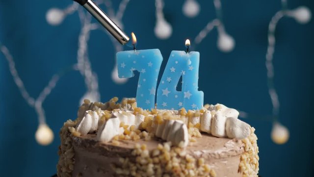 Birthday cake with 74 number candle on blue backgraund. Candles are set on fire. Slow motion and close-up view