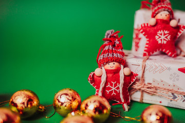Red knitted christmas stars in funny hats with golden christmas balls and white gift boxes around. Christmas dolls on the green background with copy space.
