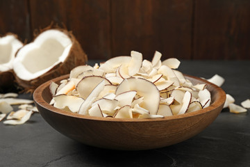 Tasty coconut chips in bowl on black table