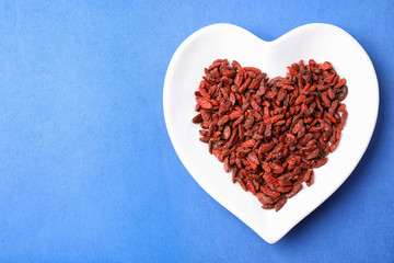 Dried goji berries in heart shaped plate on blue background, top view. Space for text