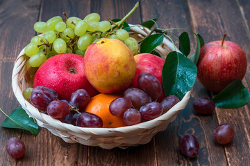 red grape berries and fresh fruits in a straw basket on a dark wooden background.