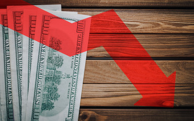 The light red arrow down icon on a wooden background with money. The concept of changing course of US dollar on the market. Devaluation, collapse, stagnation of the economy.