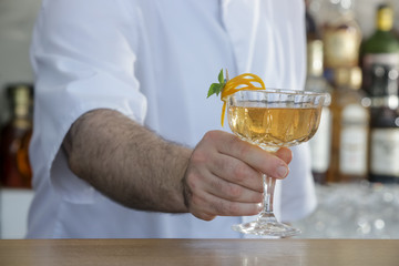 A glass of beautifully decorated whiskey cocktail with an orange peel on the bar counter