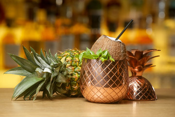 A glass of beautifully decorated pineapple coconut cocktail. Blurred bottles in the background.