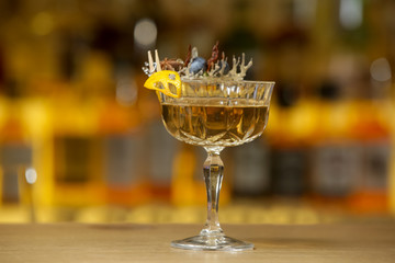 A glass of beautifully decorated whiskey cocktail with an orange peel on the bar counter