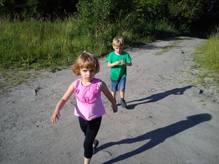Blond-haired children walk on a dirt road in the summer. Boy in a green T-shirt. Girl in a pink...