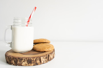 Old fashion milk jar and mason jar with red striped straws and oatmeal cookies on white background. christmas theme milk and cookies