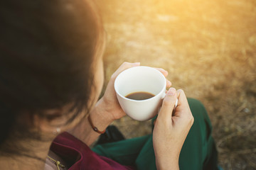 Closeup hand holding coffee cup. Woman sitting on a chair and drink coffee on the morning.