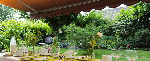feierlich in grün weiß gedeckter Tisch im Garten im Hintergrund Büsche und Bäume