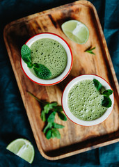 Two portions of green spinach smoothie with banana, lime and oat milk.