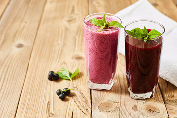Refreshing drinks in glass glasses. Milkshake and smoothie. Blackcurrant berries and green leaves on wooden background