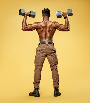 Man doing exercise with dumbbells. Photo of sporty man in training pumping up muscles of the back and hands on yellow background. Rear view. Full length © Romario Ien