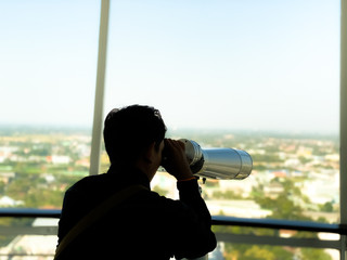 Asian tourist watching the city by binoculars with Silhouette