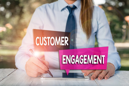 Handwriting text Customer Engagement. Conceptual photo the emotional connection between a customer and a brand Female business person sitting by table and holding mobile phone