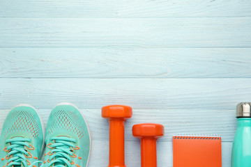 Dumbbells with notebook, shoes and bottle of water on white wooden background