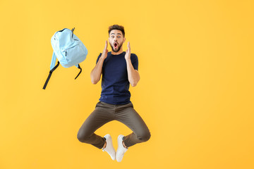 Jumping shocked young man with backpack on color background