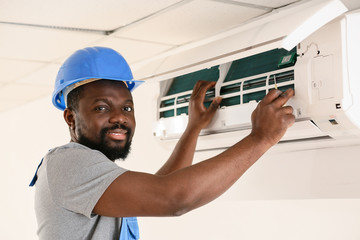 African-American electrician repairing air conditioner indoors