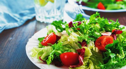 various fresh mix salad leaves with tomato in white plate on wooden background.