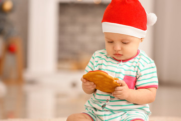 Cute little baby with Santa Claus hat and cookie on Christmas eve at home