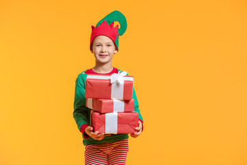 Little boy in costume of elf and with gifts on color background