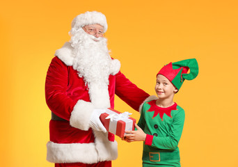Santa Claus and little elf kid with gift on color background