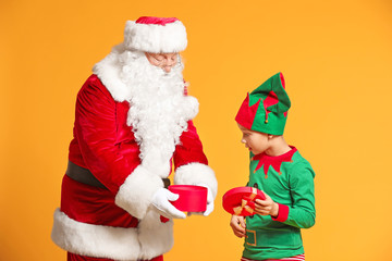 Santa Claus and little elf kid opening gift on color background