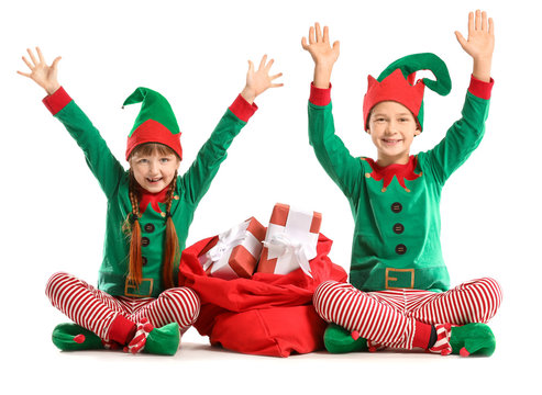 Little children in costume of elf and with Santa Claus bag full of gifts on white background