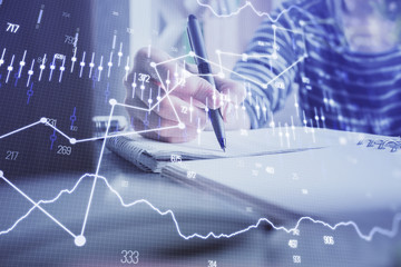 Financial forex graph drawn over hands taking notes background. Concept of research. Double exposure