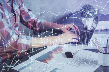 Double exposure of stock graph with businessman typing on computer in office on background. Concept of hard work.