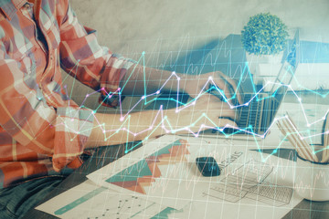 Double exposure of stock graph with businessman typing on computer in office on background. Concept of hard work.