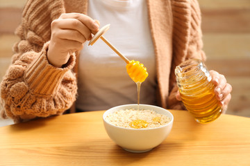 Woman adding honey to oatmeal at wooden table, closeup