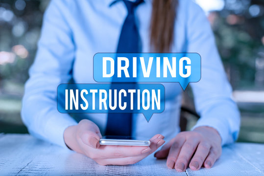 Word writing text Driving Instruction. Business photo showcasing detailed information on how driving should be done Female business person sitting by table and holding mobile phone