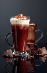 Hot chocolate with whipped cream and pieces of dark chocolate on a black background.