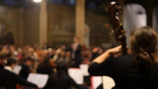 Upright bass at classical concert with musicians and conductor in the background. Soft focus.