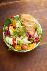 Fresh salad with tomatoes, chicken, bell peppers, radishes and mozarella cheese on wooden background. Top view flatlay with copy space