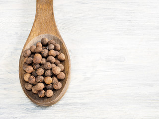 Allspice in wooden spoon on a white background. Indian cuisine, ayurveda, naturopathy, modern apothecary concept
