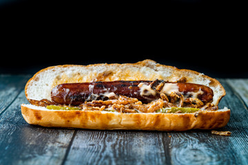 Hot Dog with Caramelized Onion, Cheddar and Gruyere Cheese Sauce on Wooden Surface with Potatoes.