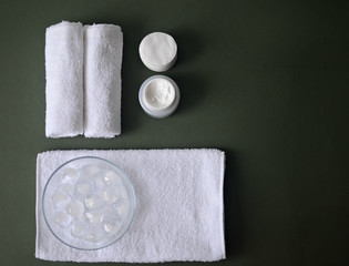 white cotton towels, face cream, cotton pads, ice cubes, spa on dark green background