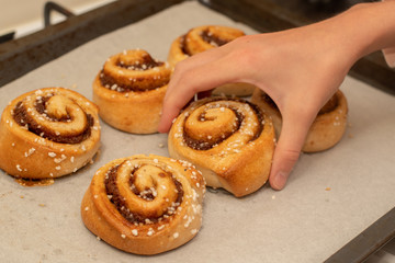 Hand taking freshly baked cinnamon buns rolls from a tray lined with baking parchment paper