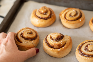 Hand taking freshly baked cinnamon buns rolls from a tray lined with baking parchment paper