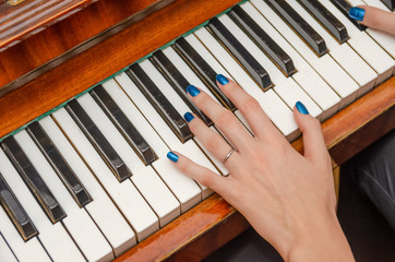hand of a young woman with blue nail Polish plays the piano close up