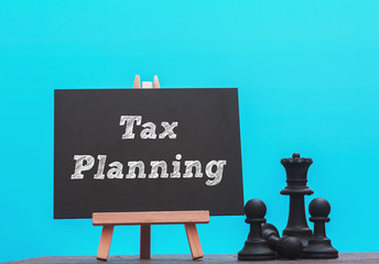 TAX PLANNING written on chalkboard with black chess on wood table,blue background conceptual